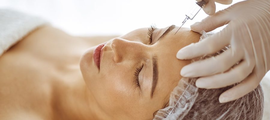 Beautician doing beauty procedure with syringe to face of young brunette woman. Cosmetic medicine and surgery, beauty injections.